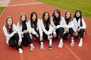 uma grupo do muitos feliz Adolescência meninas vestido dentro a mesmo equipamento tendo Diversão e posando dentro uma estádio perto uma faculdade. conceito do amizade, momentos do felicidade. escola amizade foto