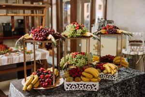 uma banquete mesa cheio do frutas e bagas, a sortimento do doces. bananas, uvas, abacaxis. fruta composições para a feriado. foto