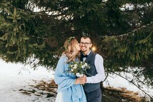 inverno Casamento dentro a montanhas. retrato do uma feliz e sorridente noiva e noivo contra a fundo do uma inverno floresta. lindo noiva e noivo ternamente abraçar. moderno inverno casamento. foto