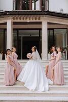 grupo retrato do a noiva e damas de honra. noiva dentro uma Casamento vestir e damas de honra dentro Rosa ou pó vestidos e segurando à moda buquês em a Casamento dia. foto