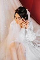 uma lindo morena noiva com uma tiara dentro dela cabelo é obtendo pronto para a Casamento dentro uma lindo roupão dentro boudoir estilo. fechar-se Casamento retrato, foto. foto