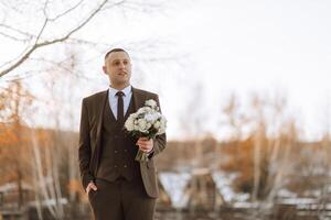 a noivo detém uma ramalhete e poses enquanto andando. inverno casamento. retrato foto