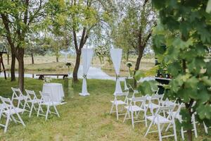 branco arco e branco cadeiras dentro a floresta para uma Casamento cerimônia. preparação. Casamento dentro natureza foto