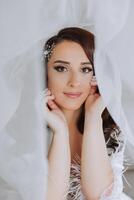 uma lindo morena noiva com uma tiara dentro dela cabelo é obtendo pronto para a Casamento dentro uma lindo roupão dentro boudoir estilo. fechar-se Casamento retrato, foto. foto