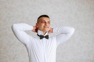 uma à moda noivo é amarrar dele gravata, preparando para a Casamento cerimônia. do noivo manhã. uma homem de negocios desgasta uma gravata. a noivo é obtendo pronto dentro a manhã antes a Casamento cerimônia. foto