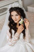 uma Maravilhoso lindo retrato do uma jovem noiva. lindo noiva com Casamento Maquiagem e joalheria guirlanda em grandes encaracolado cabelo. Casamento foto modelo com Castanho olhos dentro uma lindo interior.