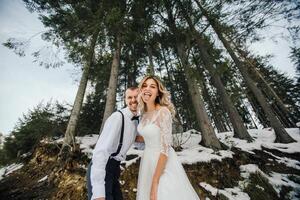 uma jovem casal, a noiva e noivo, sorrindo mostrar fora seus Casamento argolas contra a fundo do alta árvores ter uma Boa Tempo rindo. inverno Casamento foto