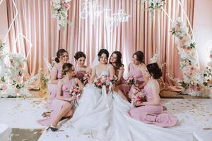 grupo retrato do a noiva e damas de honra. noiva dentro uma Casamento vestir e damas de honra dentro Rosa ou pó vestidos e segurando à moda buquês em a Casamento dia. foto