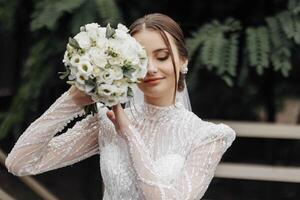 a noiva dentro uma branco Casamento vestir bordado com pedras e miçangas detém uma Casamento ramalhete do rosas e vegetação. à moda Casamento ramalhete. foto