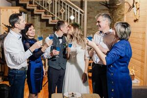 a noiva e noivo comemoro seus Casamento com seus pais dentro uma de madeira casa dentro a montanhas. moderno casamento. elas elevado seus óculos. foto