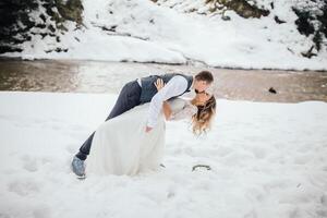 lindo casal dentro a inverno pinho floresta perto a rio, desfrutando a beleza. a noivo detém dele noiva dentro dele braços. Largo ângulo foto. inverno Casamento foto