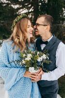 inverno Casamento dentro a montanhas. retrato do uma feliz e sorridente noiva e noivo contra a fundo do uma inverno floresta. lindo noiva e noivo ternamente abraçar. moderno inverno casamento. foto