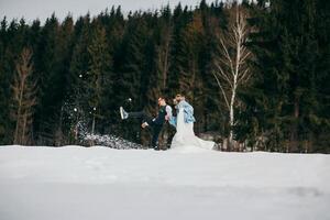 jovem casal noiva e noivo jogando dentro a inverno natureza em a fundo do a floresta. elas corre e lançar neve. pular. ter uma Boa Tempo rindo. a conceito do uma inverno Casamento dentro a montanhas foto