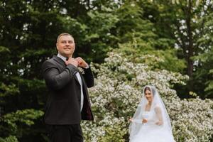 uma bonito noivo dentro a Primavera floresta carrinhos dentro frente do dele noiva. lindo Casamento branco vestir. anda em dentro a parque. uma feliz e amoroso casal. foto