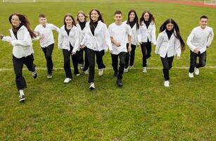 uma grupo do muitos feliz adolescentes vestido dentro a mesmo equipamento tendo Diversão e posando dentro uma estádio perto uma faculdade. conceito do amizade, momentos do felicidade. escola amizade foto