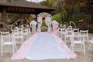 Casamento decoração. muitos branco cadeiras e uma branco caminho. uma branco e Rosa arco decorado com flores preparação para a Casamento cerimônia. celebração foto