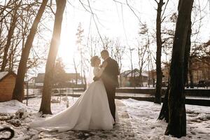 inverno casamento. uma feliz casal dentro Casamento roupas estão abraçando e sorridente dentro uma inverno parque coberto com neve em seus Casamento dia. inverno amor história do uma lindo casal dentro Nevado inverno clima foto