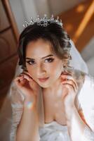 uma lindo morena noiva com uma tiara dentro dela cabelo é obtendo pronto para a Casamento dentro uma lindo roupão dentro boudoir estilo. fechar-se Casamento retrato, foto. foto