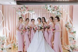 grupo retrato do a noiva e damas de honra. noiva dentro uma Casamento vestir e damas de honra dentro Rosa ou pó vestidos e segurando à moda buquês em a Casamento dia. foto