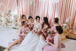 grupo retrato do a noiva e damas de honra. noiva dentro uma Casamento vestir e damas de honra dentro Rosa ou pó vestidos e segurando à moda buquês em a Casamento dia. foto