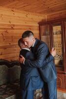 uma pai abraços dele maduro filho e ajuda ele preparar para a Casamento cerimônia. caloroso e sincero relações entre uma pai e a adulto filho. a emocional momento às uma Casamento foto