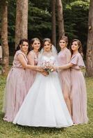 grupo retrato do a noiva e damas de honra. noiva dentro uma Casamento vestir e damas de honra dentro Rosa ou pó vestidos e segurando à moda buquês em a Casamento dia. foto