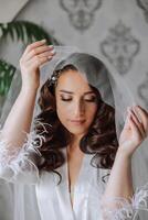 uma lindo morena noiva com uma tiara dentro dela cabelo é obtendo pronto para a Casamento dentro uma lindo roupão dentro boudoir estilo. fechar-se Casamento retrato, foto. foto