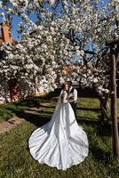 casamento. amor e casal dentro jardim para casamento. celebração do cerimônia e compromisso. Salve  a data. confiar. a noiva e noivo abraçar. a noivo abraços a noiva debaixo uma Primavera floração árvore. foto