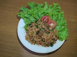 delicioso indonésio frito arroz nasi Goreng com grande quantidade do alface, mostarda verduras e tomates servido em uma branco prato foto