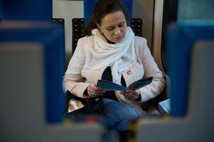 confiante jovem empresária 40. anos velho, desfrutando dela o negócio viagem, lendo folheto enquanto pendulares para trabalhos em alta velocidade confortável trem. pessoas. negócios. Ferrovia transporte. estilo de vida foto