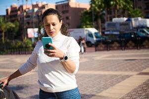 jovem mulher verificação inteligente telefone em a rua, reserva Táxi ou procurando geolocalização em conectados mapas em Móvel aplicativo foto