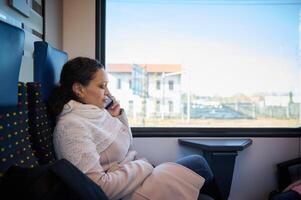 jovem mulher r falando em inteligente Móvel telefone enquanto viajando de trem. fêmea passageiro equitação uma trem. pessoas. viagem foto