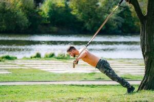 uma Forte homem abraçando da natureza força. uma sem camisa homem segurando para uma pólo dentro uma parque foto