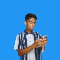 jovem ásia homem surpreso olhando às inteligente telefone, vestindo colorida camiseta, azul fundo foto