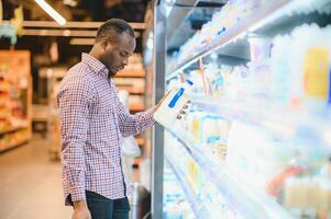 africano homem compras às supermercado. bonito cara segurando compras cesta foto