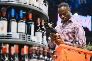 africano americano homem dentro uma supermercado escolhendo uma vinho foto