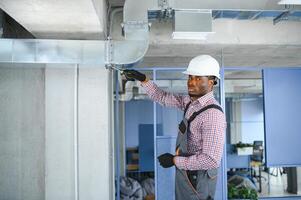 hvac africano trabalhador instalar canalizado tubo sistema para ventilação e ar condicionamento. cópia de espaço foto