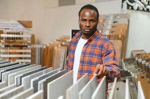 africano americano homem cliente escolhendo cerâmico telha às construção materiais loja foto