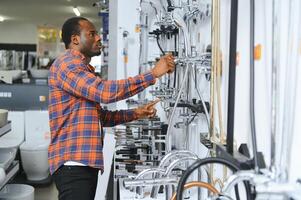 africano homem dentro uma Castanho casaco escolhe uma banheiro torneira dentro uma construção supermercado, encanamento reparos dentro a casa foto