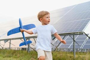 pequeno feliz Garoto jogando com brinquedo avião perto solar painéis. foto