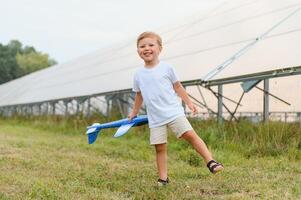 pequeno feliz Garoto jogando com brinquedo avião perto solar painéis. foto