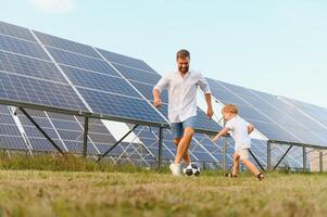 pai e filho ter Diversão jogando futebol perto a solar painéis. a conceito do verde energia foto