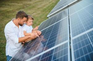 homem mostrando pequeno criança a solar painéis durante ensolarado dia. pai apresentando para dele criança moderno energia recurso. pequeno passos para alternativo energia. foto