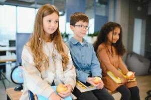 multirracial escolares tendo almoço às a escrivaninha durante uma pausa dentro escola foto