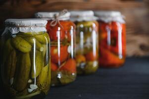 vidro frascos com em conserva pepinos picles, em conserva tomates e repolho. frascos do vários em conserva legumes. enlatado Comida dentro uma rústico composição. foto