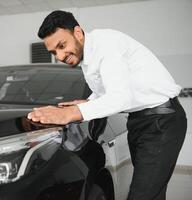 uma jovem indiano homem escolhe uma Novo carro às uma carro concessionária foto