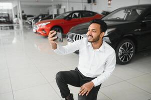 bonito indiano homem levando uma selfie com carro chaves para dele Novo automóvel às a concessionária sala de exposições copyspace tecnologia social meios de comunicação partilha positividade estilo de vida viajando turismo. foto