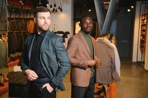 dois à moda multirracial homens em pé dentro clássico ternos em pé dentro uma roupas loja foto