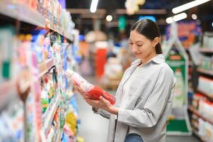 interessado jovem mulher fazer compras dentro família produtos químicos loja, lendo etiquetas em garrafas foto