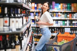 jovem mulher decidir o que vinho para Comprar dentro supermercado foto